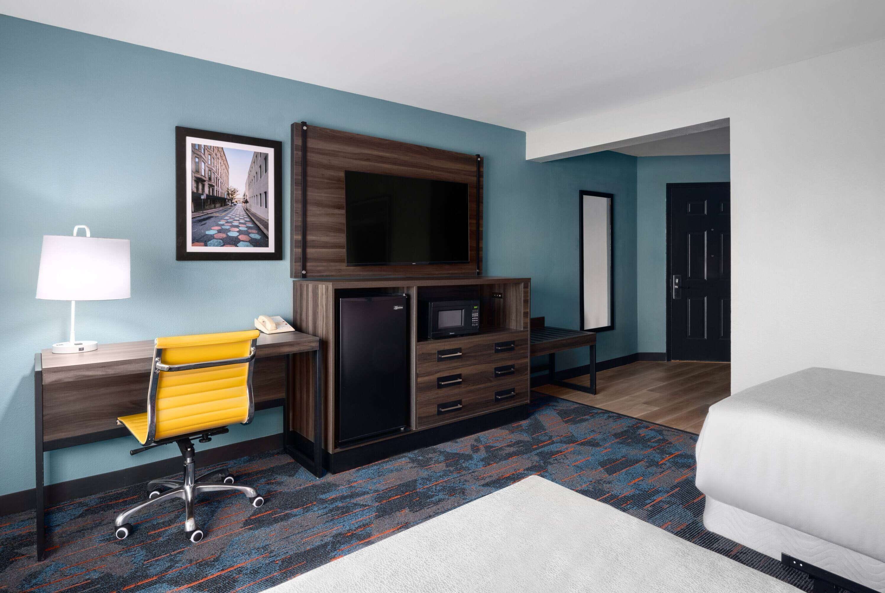 Une chambre d’hôtel équipée d’un bureau, d’une chaise, d’un lit, d’une télévision et d’un four à micro-ondes.