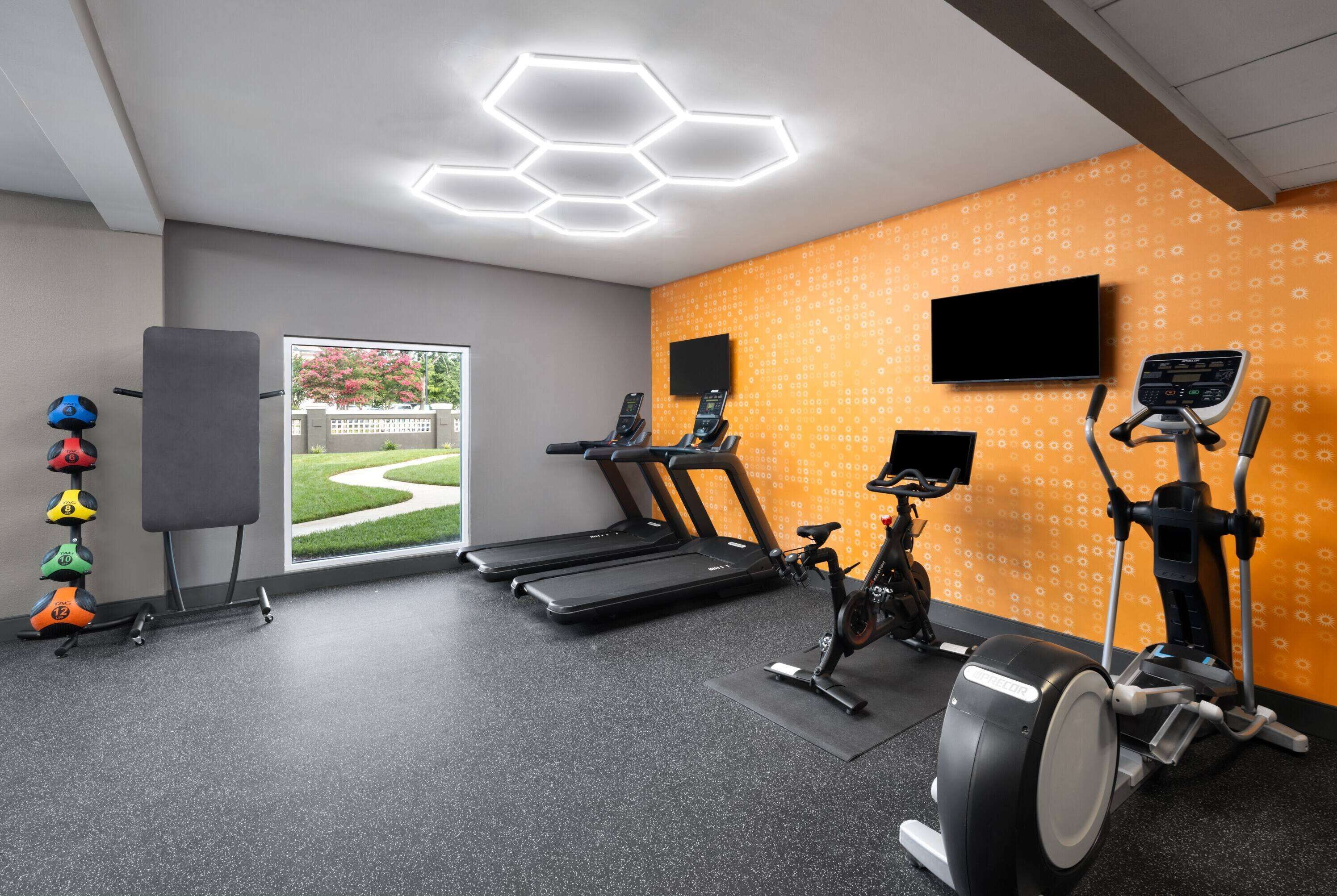 Un gimnasio con cintas de correr, una elíptica y una bicicleta estática. Hay un ventanal con vistas a un jardín.