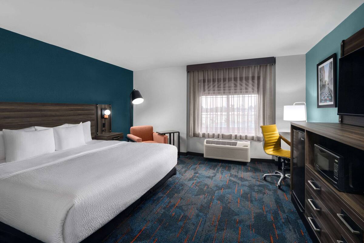 A hotel room with a large bed, a desk, a chair, a TV, and a window with curtains.