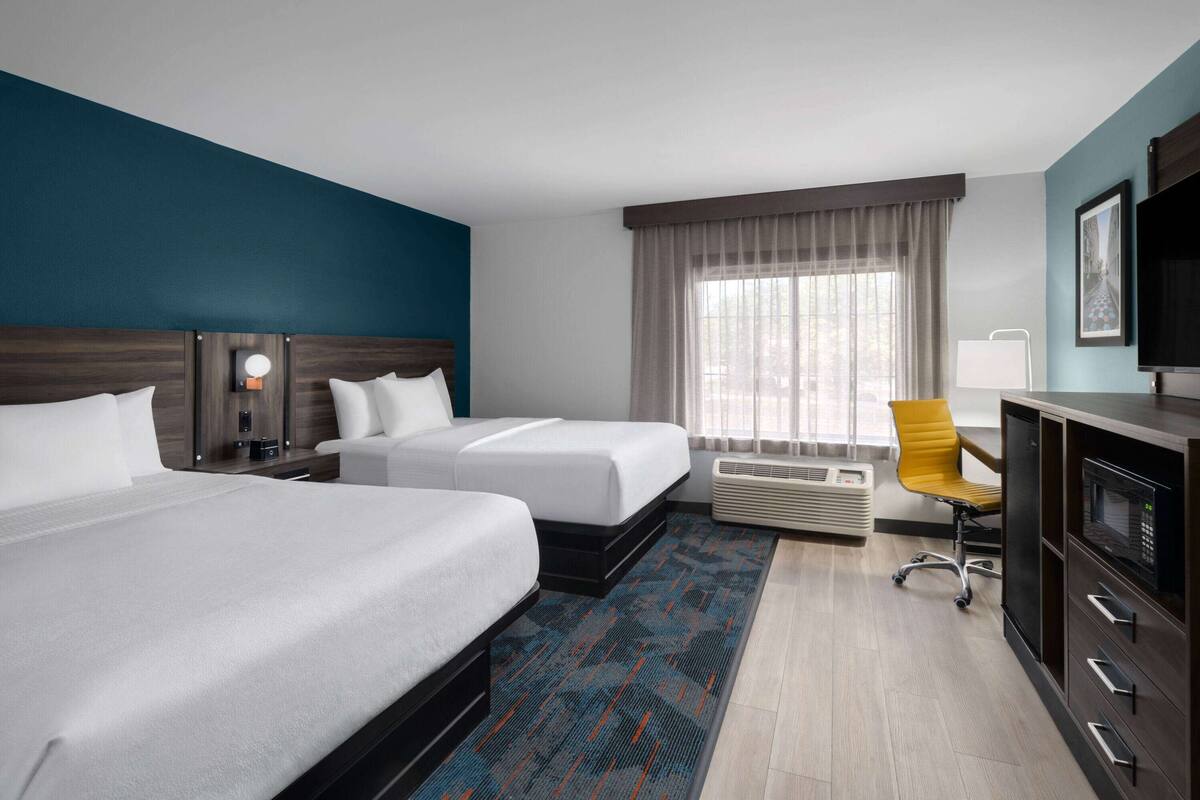 A hotel room with two beds, a desk with a TV, a chair, and a window with curtains.