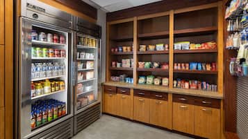 A kitchenette with a refrigerator stocked with beverages and a pantry with various food items.