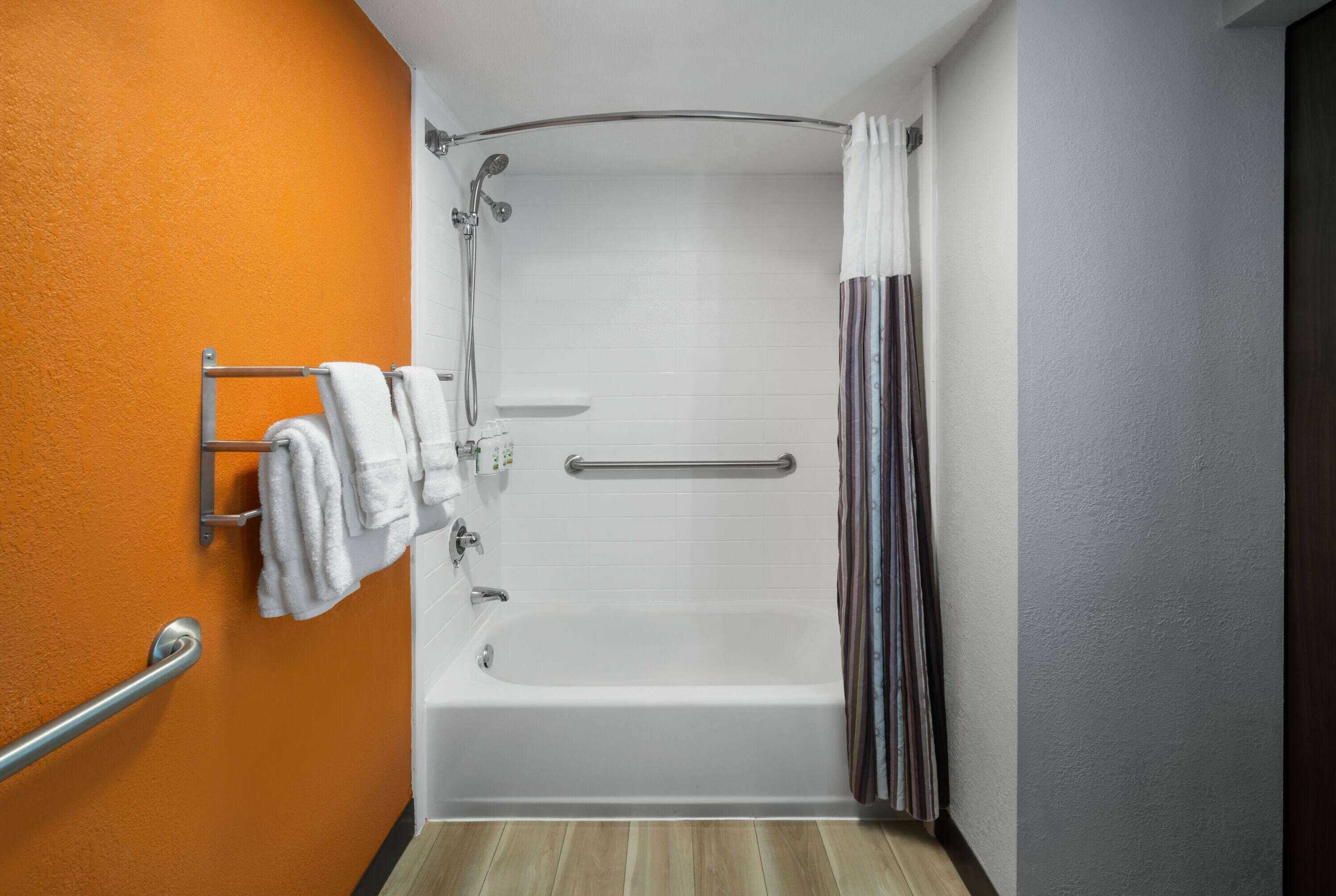 A bathroom with an orange wall, a white bathtub, and a shower area with a glass door.