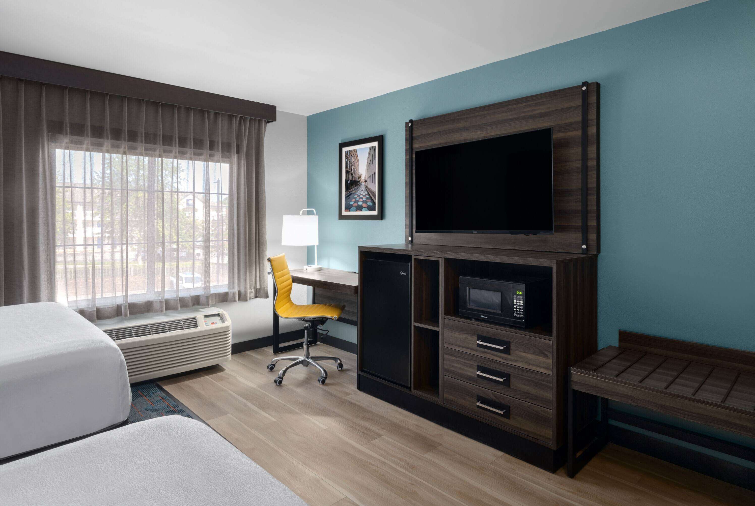 A hotel room with a bed, a desk with a chair, a TV, a microwave, and a small seating area.