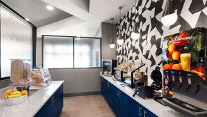 Un espacio moderno de cocina con estación de café, exposición de frutas y pared decorada.