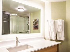 A bathroom with a large mirror, a sink, a shower, and two towels hanging on the wall.