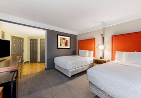 A hotel room with two beds, a desk, a television, and a framed picture on the wall.