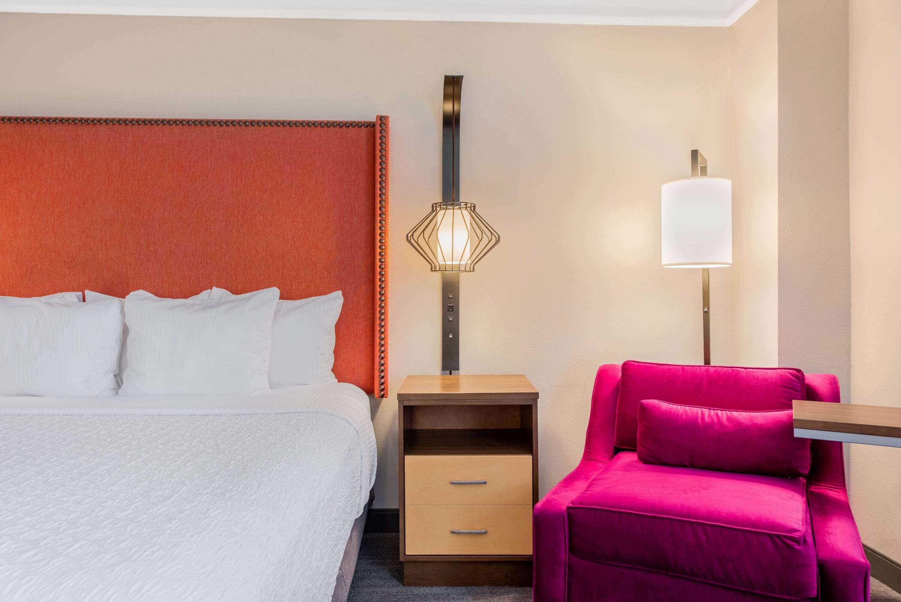Une chambre d’hôtel comprenant un lit, une table de chevet avec une lampe, une chaise et une étagère fixée au mur.