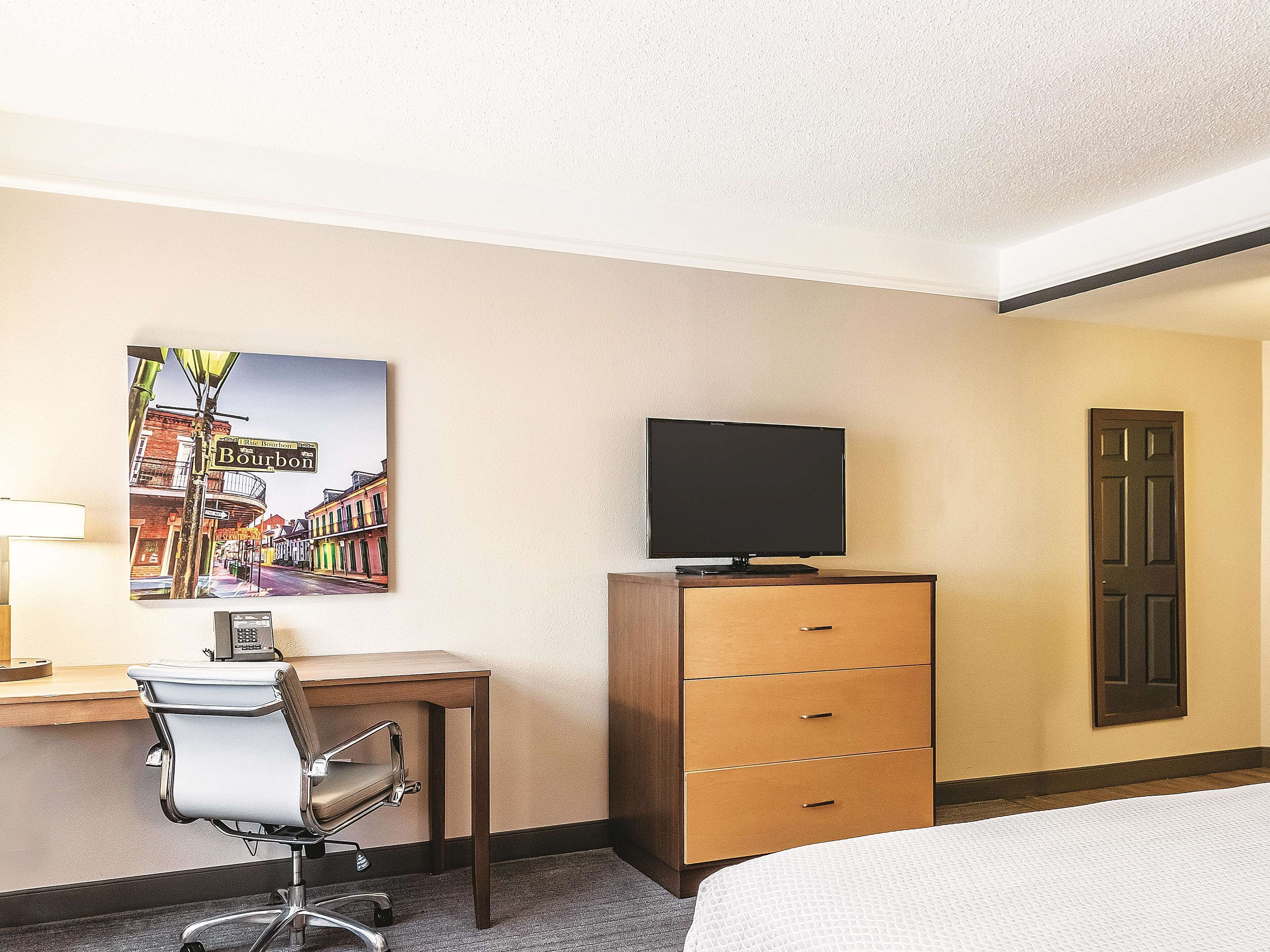 Ein Hotelzimmer mit Bett, Schreibtisch mit Stuhl, Fernseher auf einer Kommode und einem Bild an der Wand.