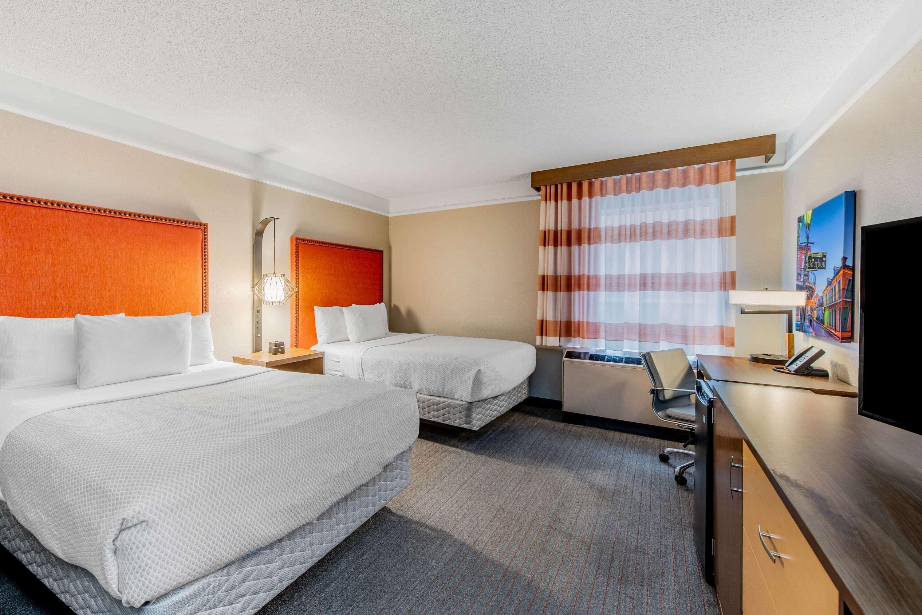A hotel room with two beds, a desk, a chair, a television, and a window with curtains.