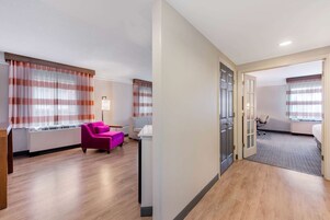 Habitación de hotel con piso de madera, una silla rosa, un escritorio con lámpara y una cama.