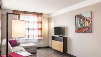 A living room with a sofa, ottoman, lamp, TV, and a painting on the wall.