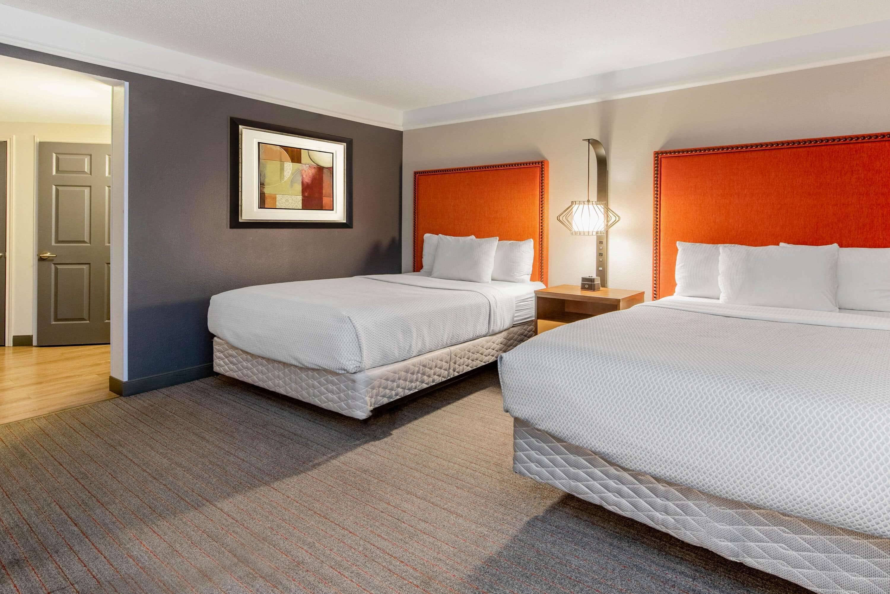 A hotel room with two beds, a framed picture on the wall, and a nightstand with a lamp.