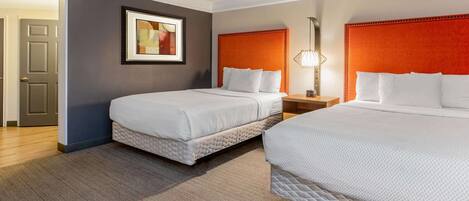 A hotel room with two beds, a framed picture on the wall, and a nightstand with a lamp.