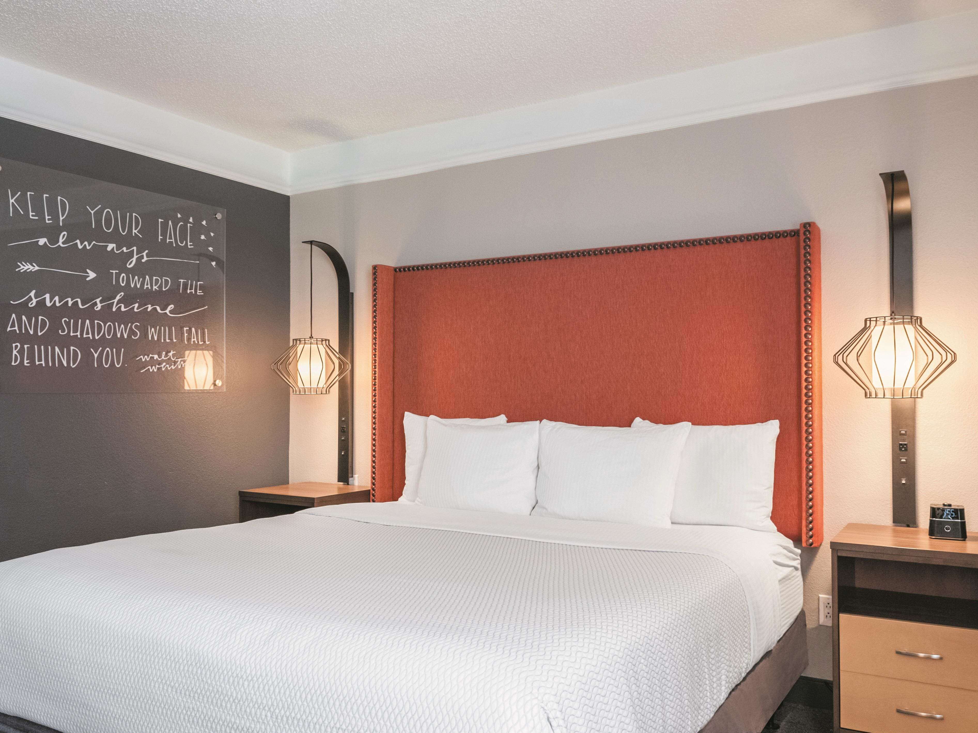 A neatly made bed with white linens, a red upholstered headboard, and two bedside lamps.