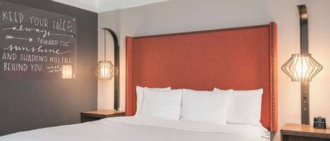 A neatly made bed with white linens, a red upholstered headboard, and two bedside lamps.