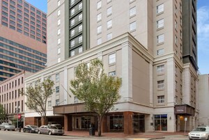 Un hotel de varios pisos con una fachada clásica, grandes ventanales y un árbol en primer plano.