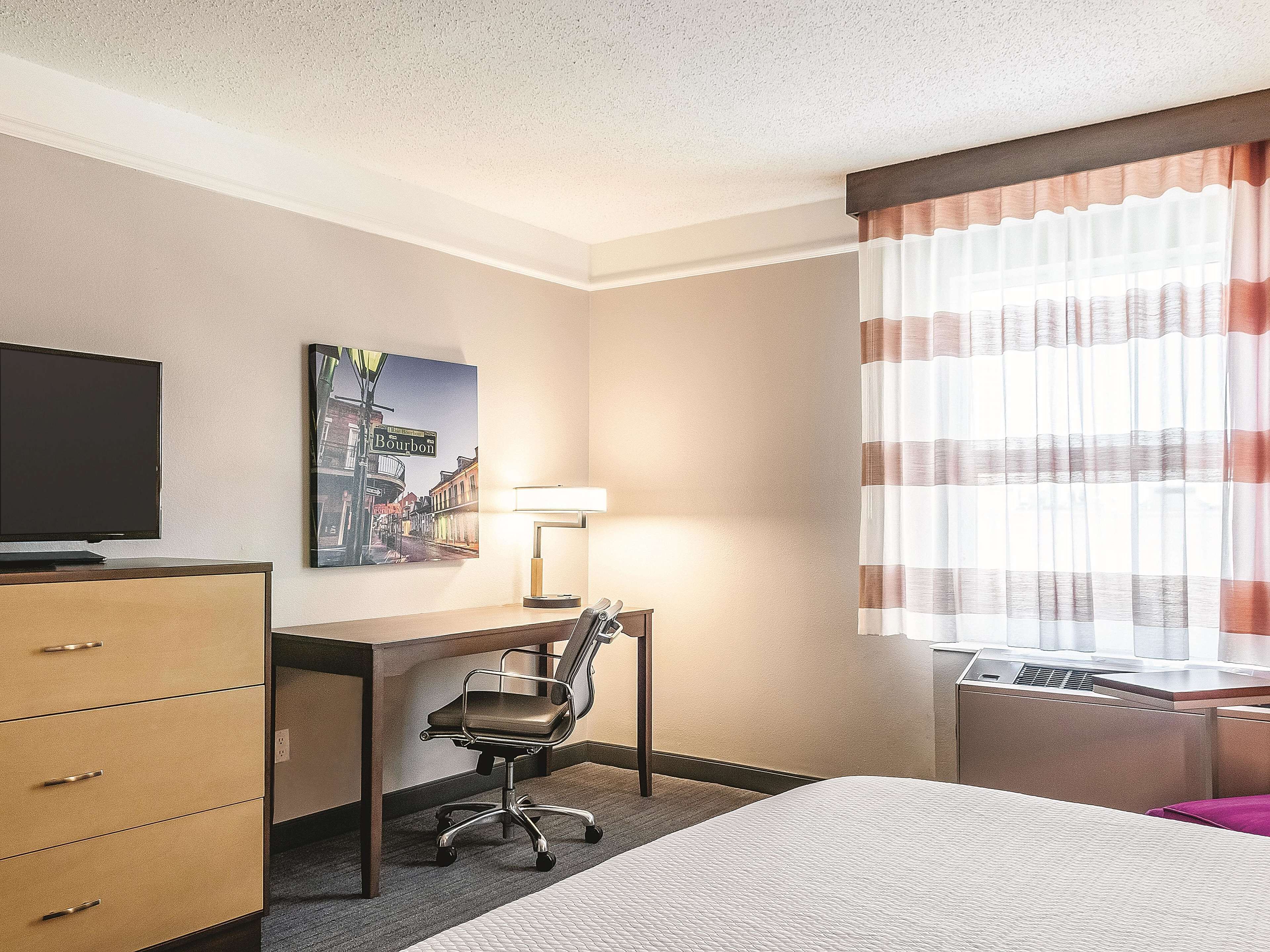 A hotel room with a bed, desk, chair, TV, lamp, and a window with curtains.