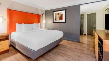 A modern hotel room with a large bed, wooden flooring, a red accent wall, and a framed artwork above the bed.