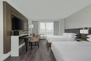 Quarto de hotel com cama, escrivaninha, cadeira, televisão e janela com cortinas.