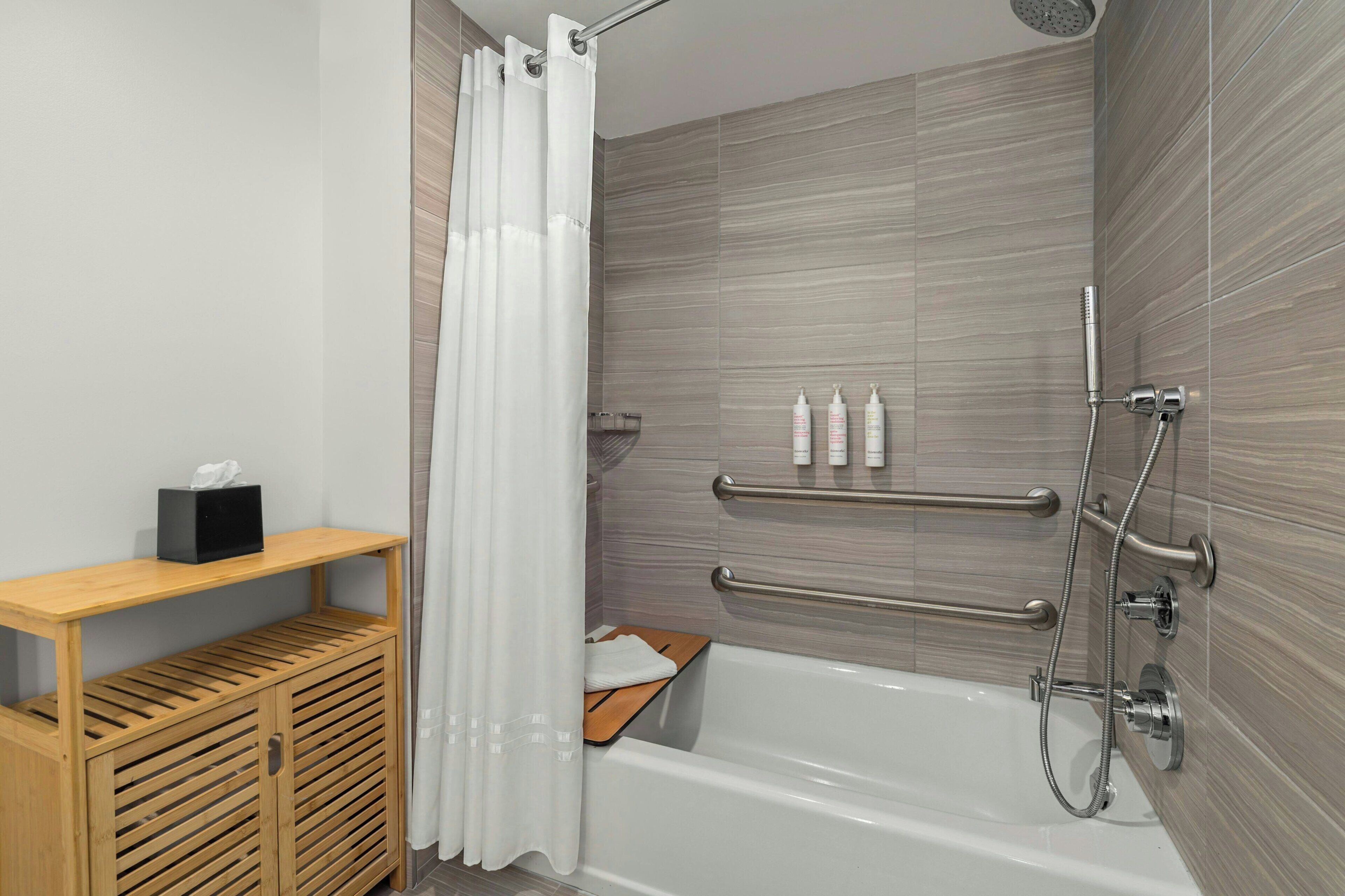 A modern bathroom with a bathtub, shower, and a wooden shelf with toiletries.