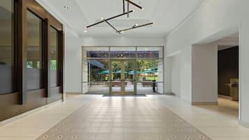 Un hall amplio con diseño moderno, que cuenta con una entrada de vidrio grande, piso con diseño y techo con vigas y luminarias a la vista.