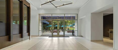 Un hall amplio con diseño moderno, que cuenta con una entrada de vidrio grande, piso con diseño y techo con vigas y luminarias a la vista.