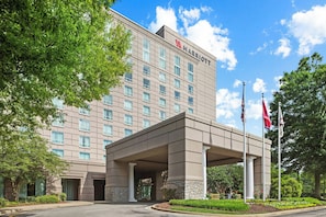A multi-story hotel with a prominent entrance, flagpoles, and a landscaped area with trees and shrubs.