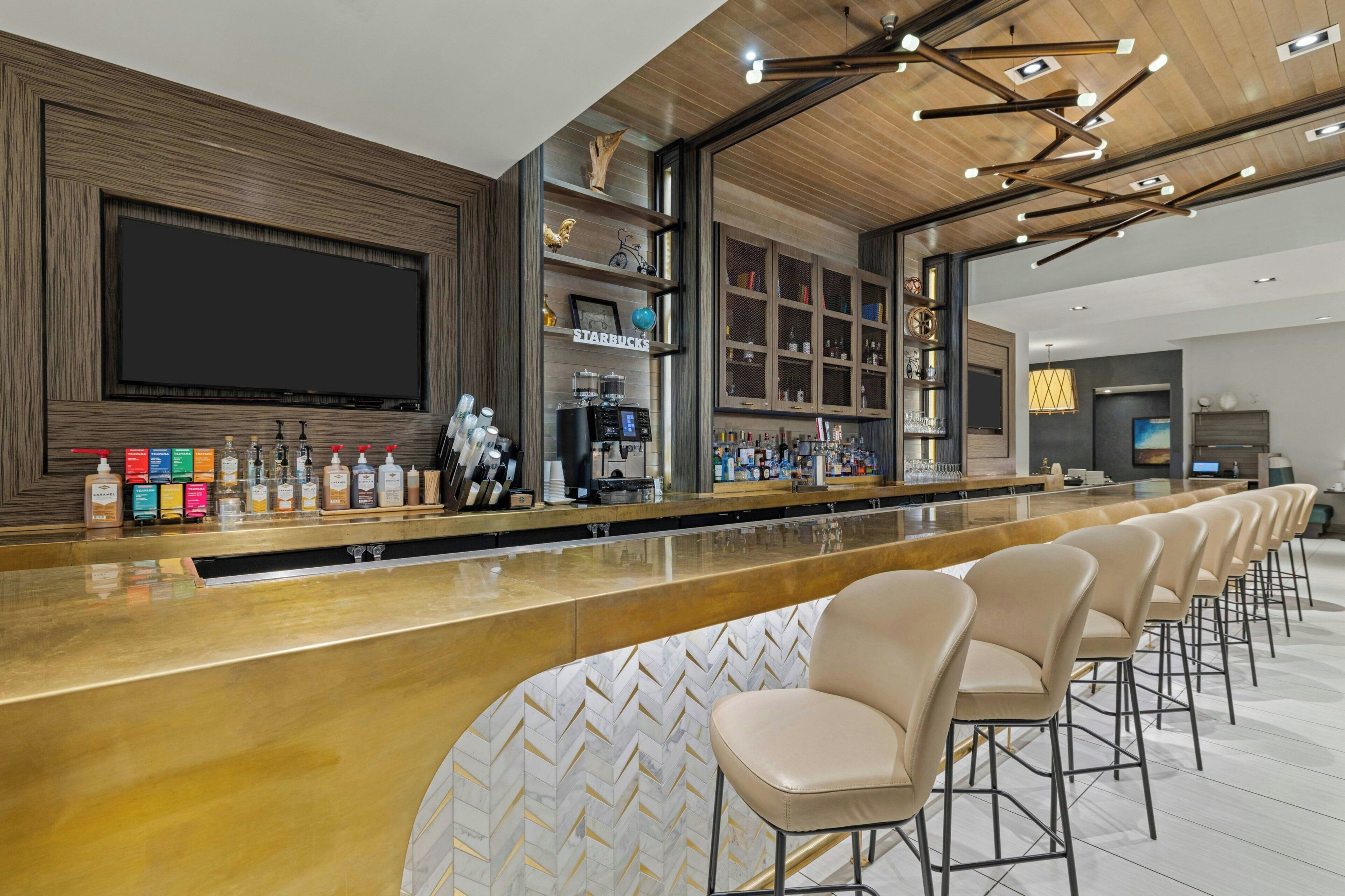 A modern bar area with a long counter, bar stools, and a large flat-screen TV mounted on the wall.