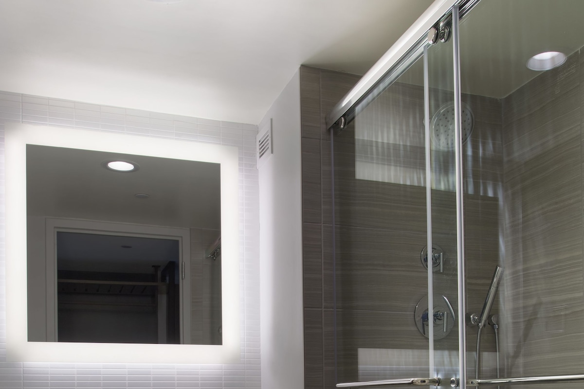 A modern bathroom with a glass-enclosed shower, a large mirror, and a vanity with a towel rack.