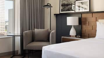 A hotel room with a bed, a chair, a desk, a lamp, and two framed pictures on the wall.