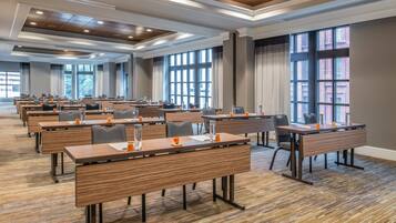 A conference room with multiple tables and chairs, large windows, and a wooden floor.