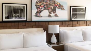 A hotel room with a bed, a nightstand, a lamp, and two framed artworks on the wall.