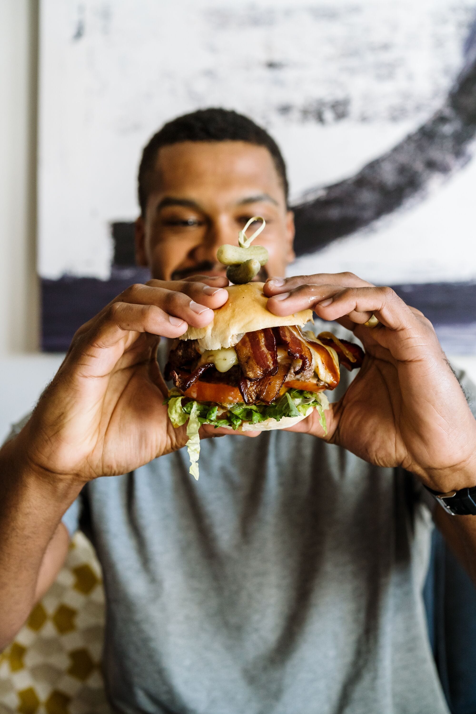 A person holding a burger with visible lettuce, tomato, and bacon.