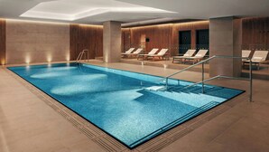 A modern indoor swimming pool with clear water, surrounded by lounge chairs and a wooden wall. - Prague Marriott Hotel (Prague)