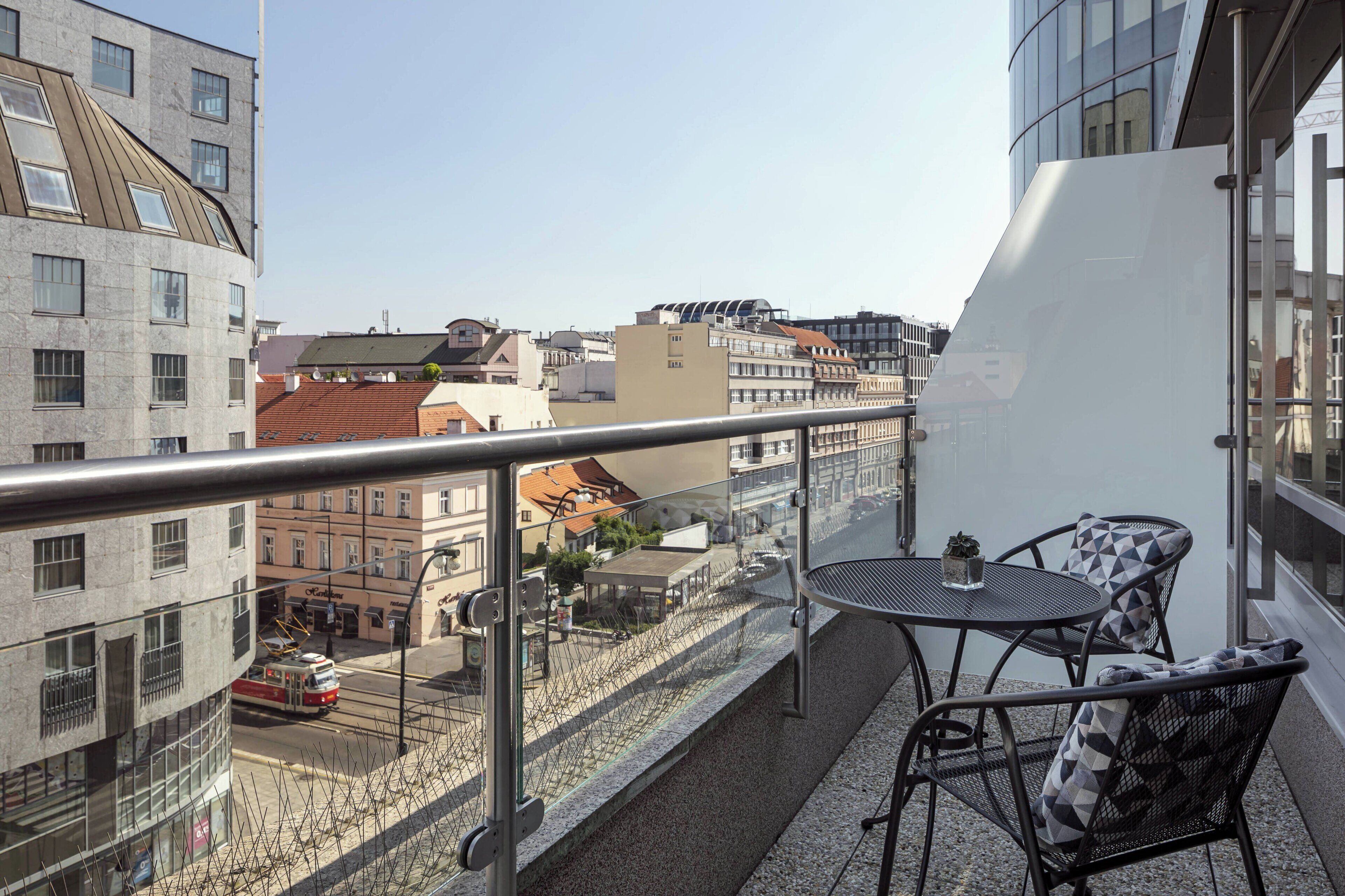 A balcony with a metal railing, a round table, and two chairs with patterned cushions.