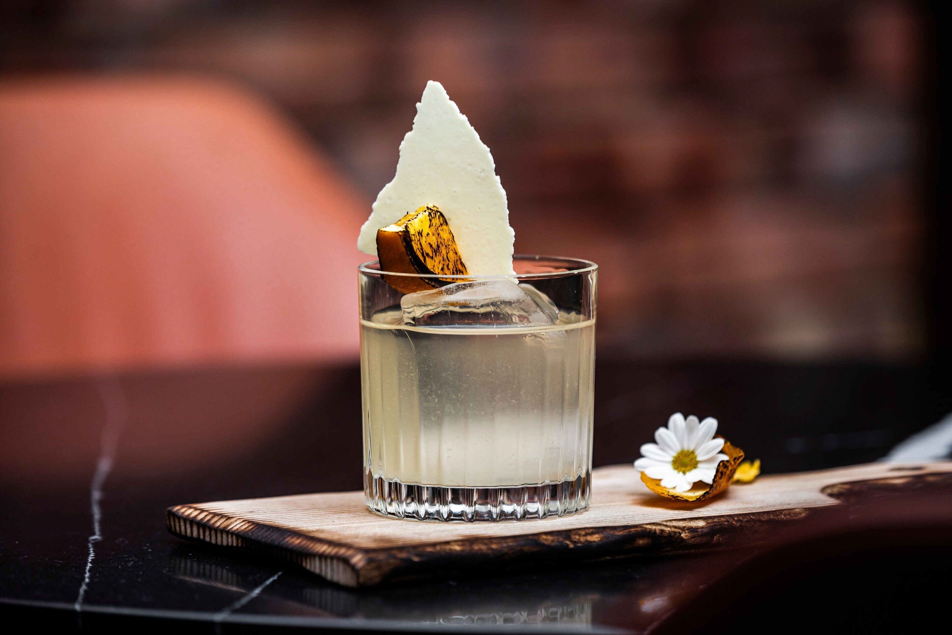 A clear glass with a layered drink, ice, and a decorative element on a coaster.