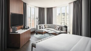 Una habitación de hotel moderna con una cama grande, un sofá, un escritorio y un televisor de pantalla plana, y vistas a la ciudad.