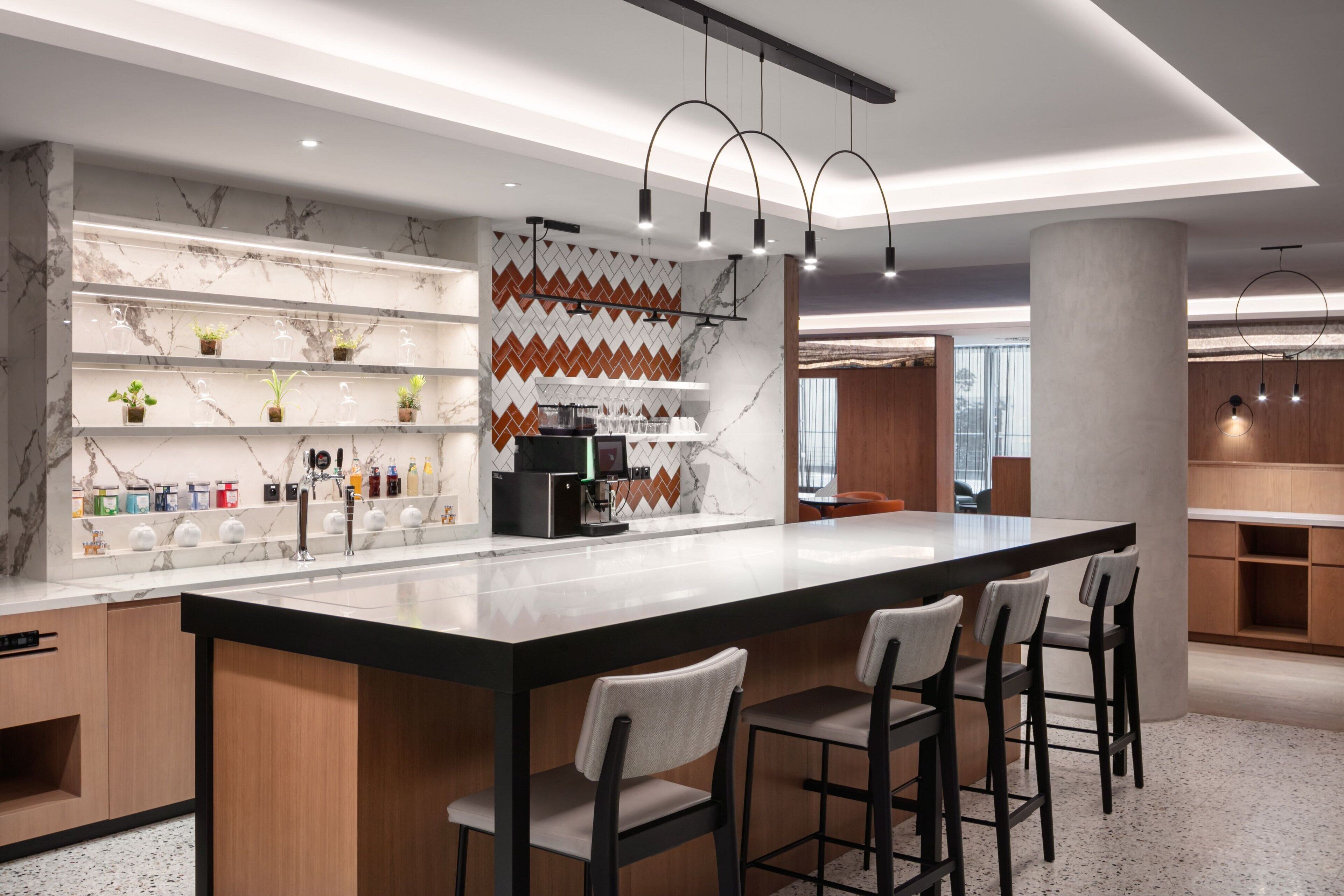 A modern kitchen with a marble backsplash, a coffee machine, and bar stools.
