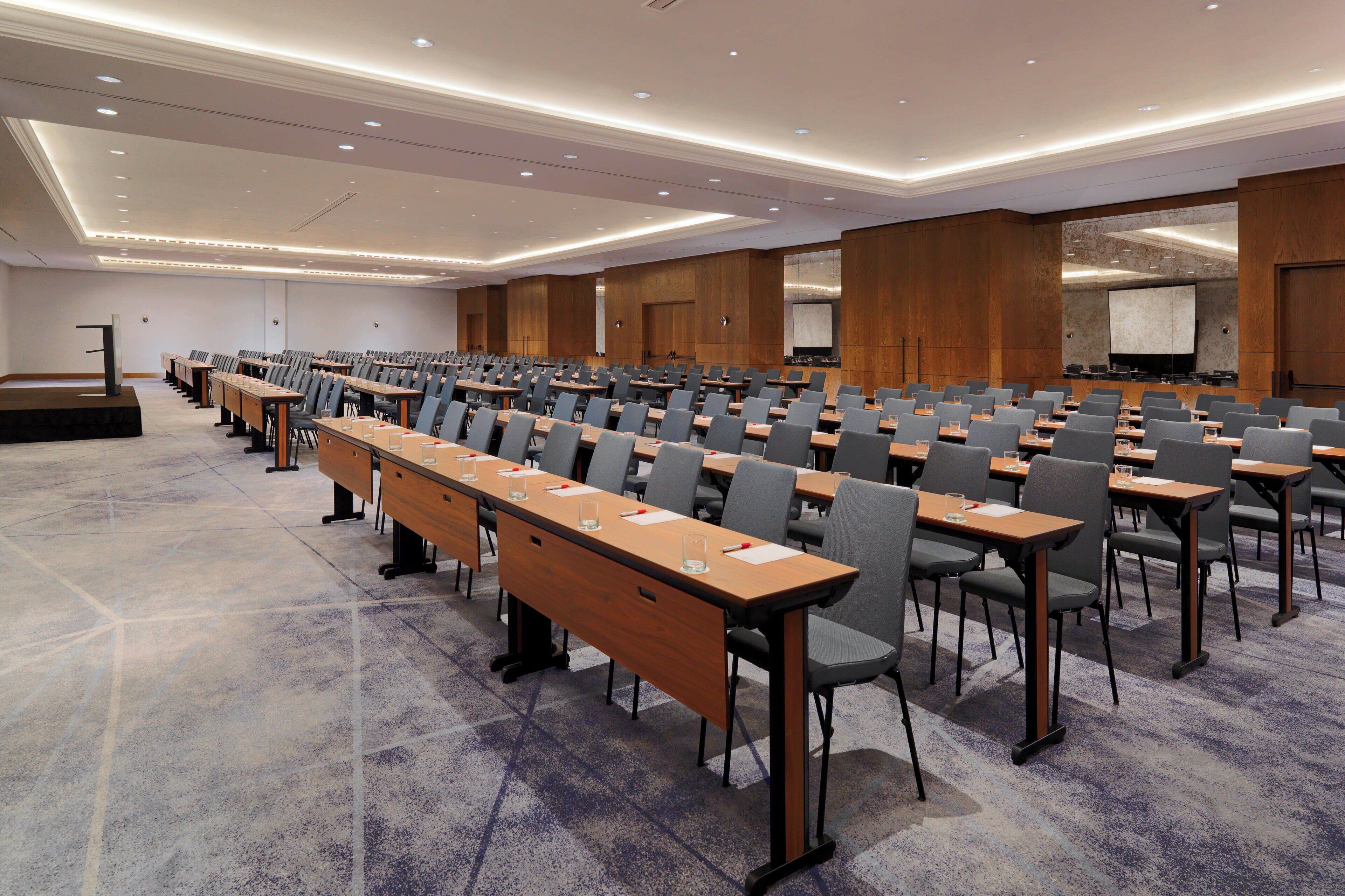 A conference room with rows of tables and chairs, a podium, and a projection screen.