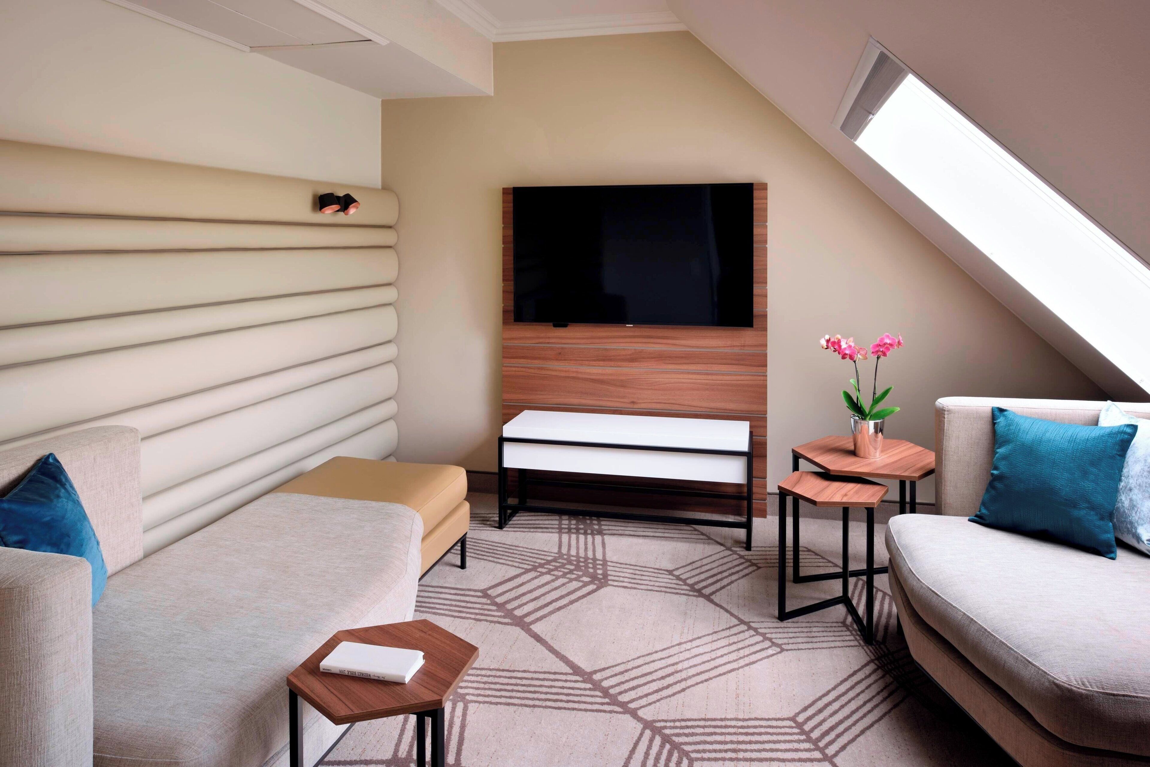 A modern, well-lit room with a sofa, a small table, a bench, and a TV mounted on a wooden wall.