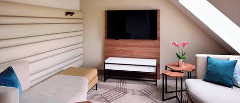 A modern, well-lit room with a sofa, a small table, a bench, and a TV mounted on a wooden wall.