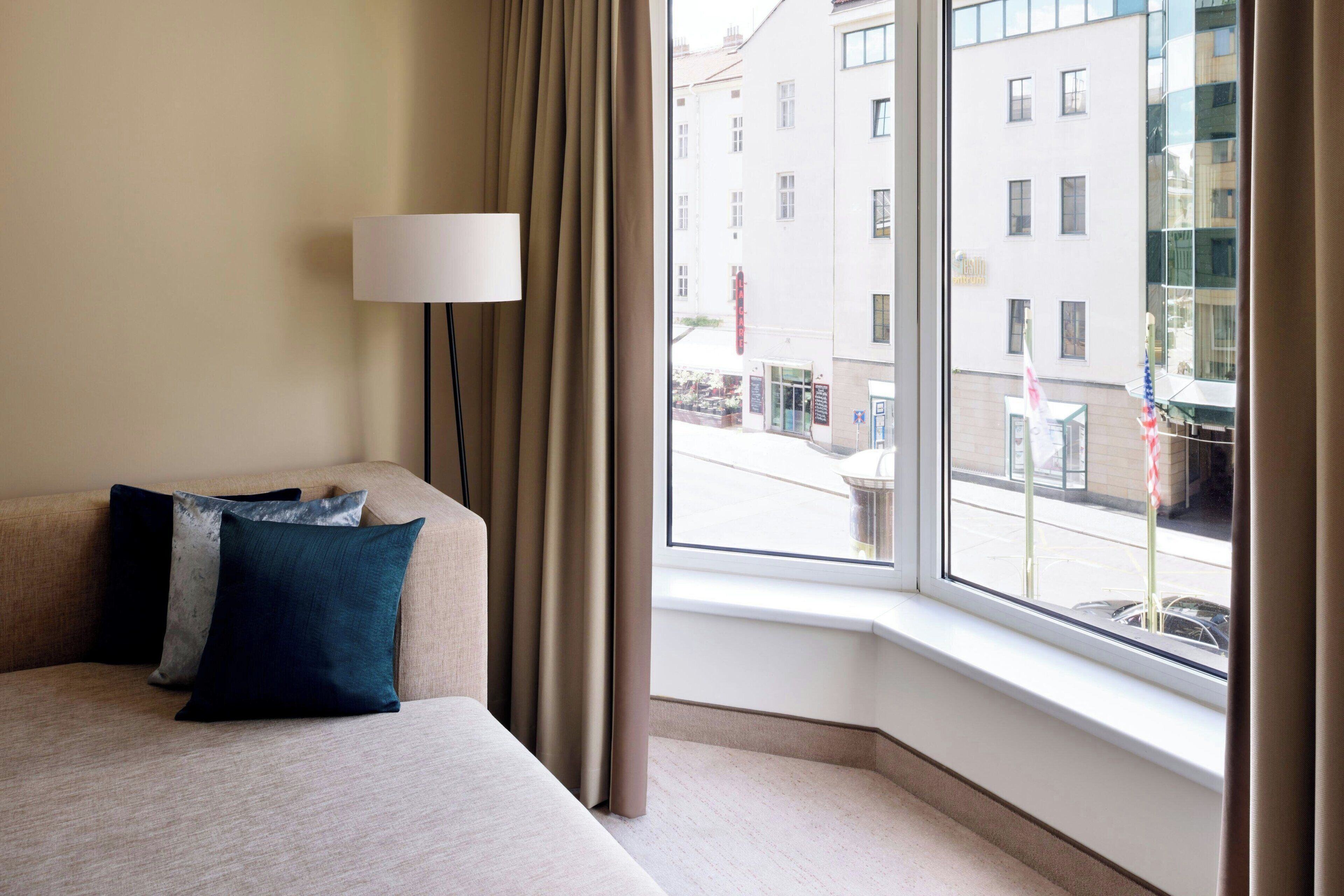 Habitación de hotel con cama, lámpara y ventana con vistas a edificios.