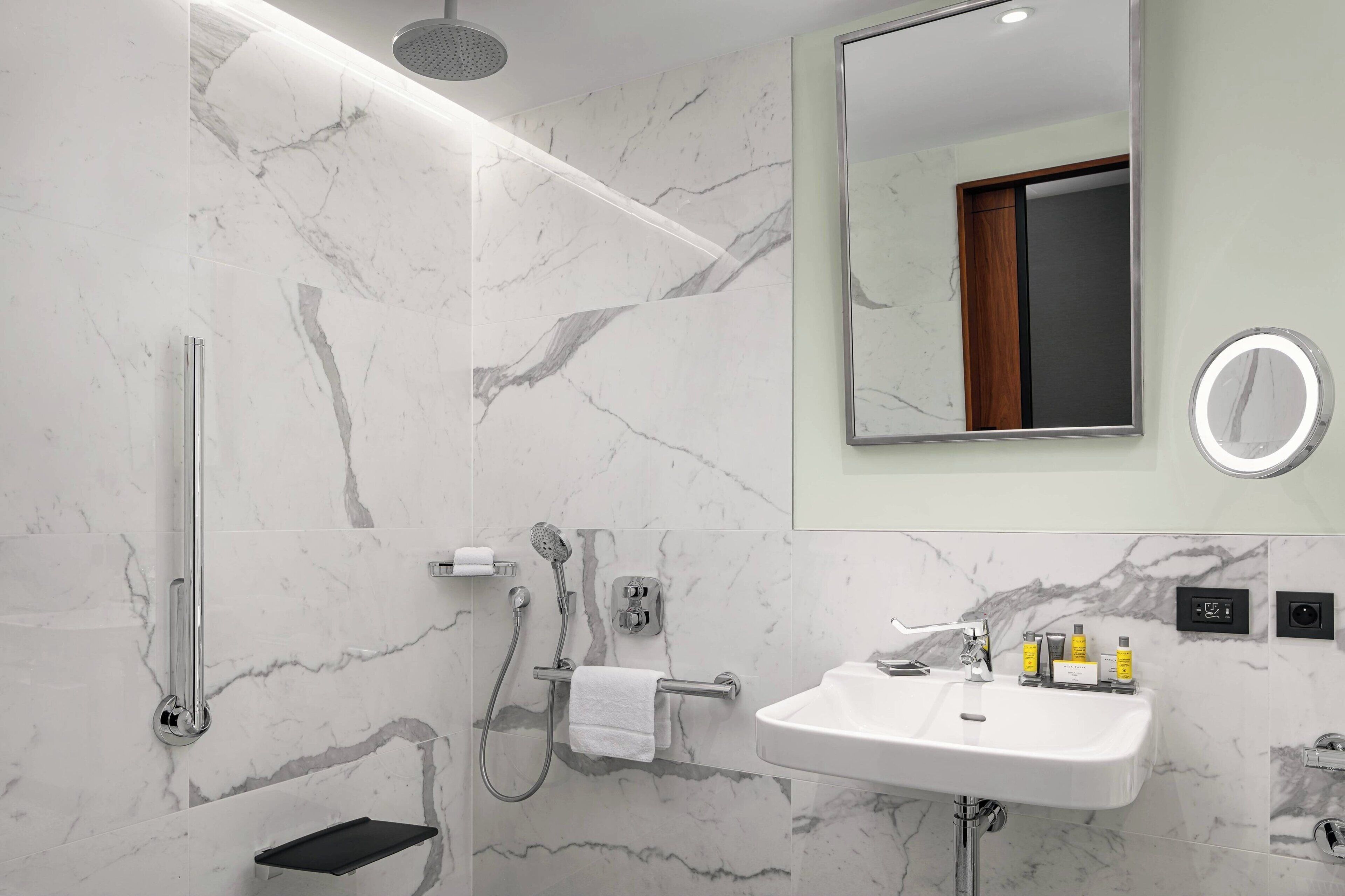 Un baño moderno con pared de mármol, ducha, lavamanos y espejo.
