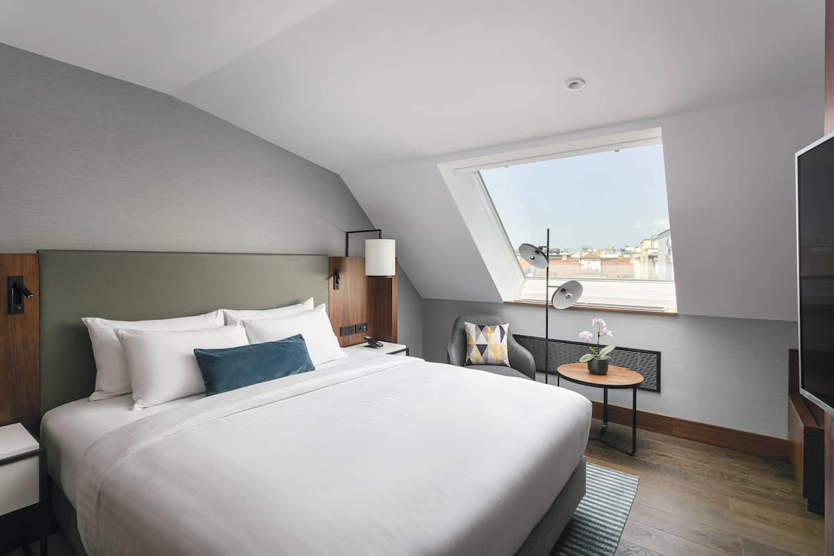 Une chambre d’hôtel moderne équipée d’un grand lit, d’un bureau, d’une chaise, d’une télévision et d’une fenêtre de toit.