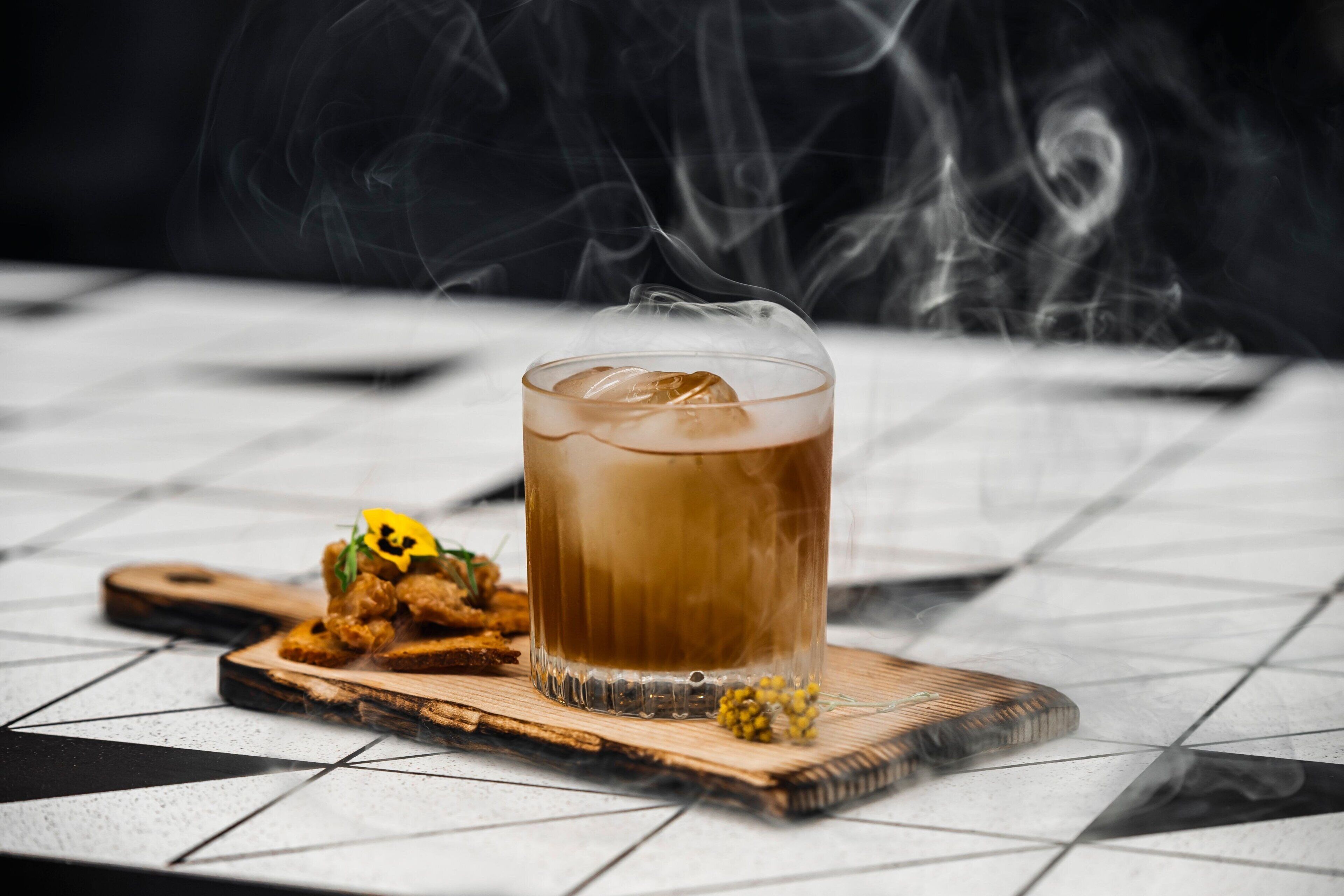 A glass of iced beverage on a wooden coaster with a square tile table.