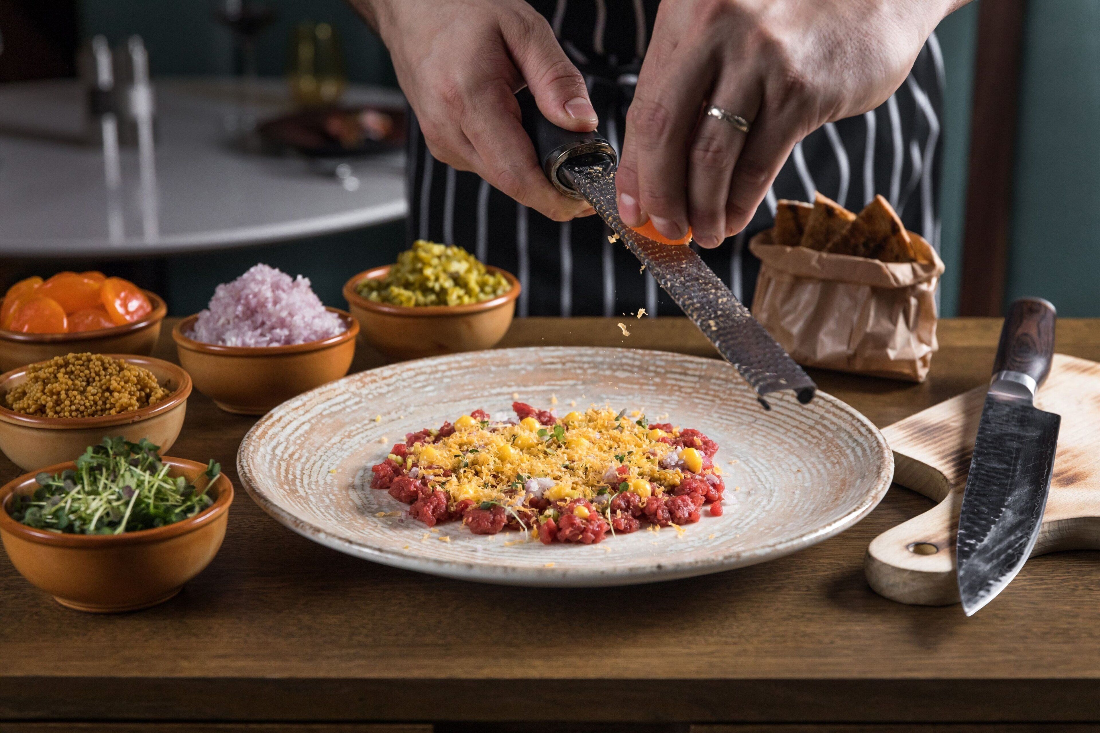 A person grating cheese over a dish with various ingredients.