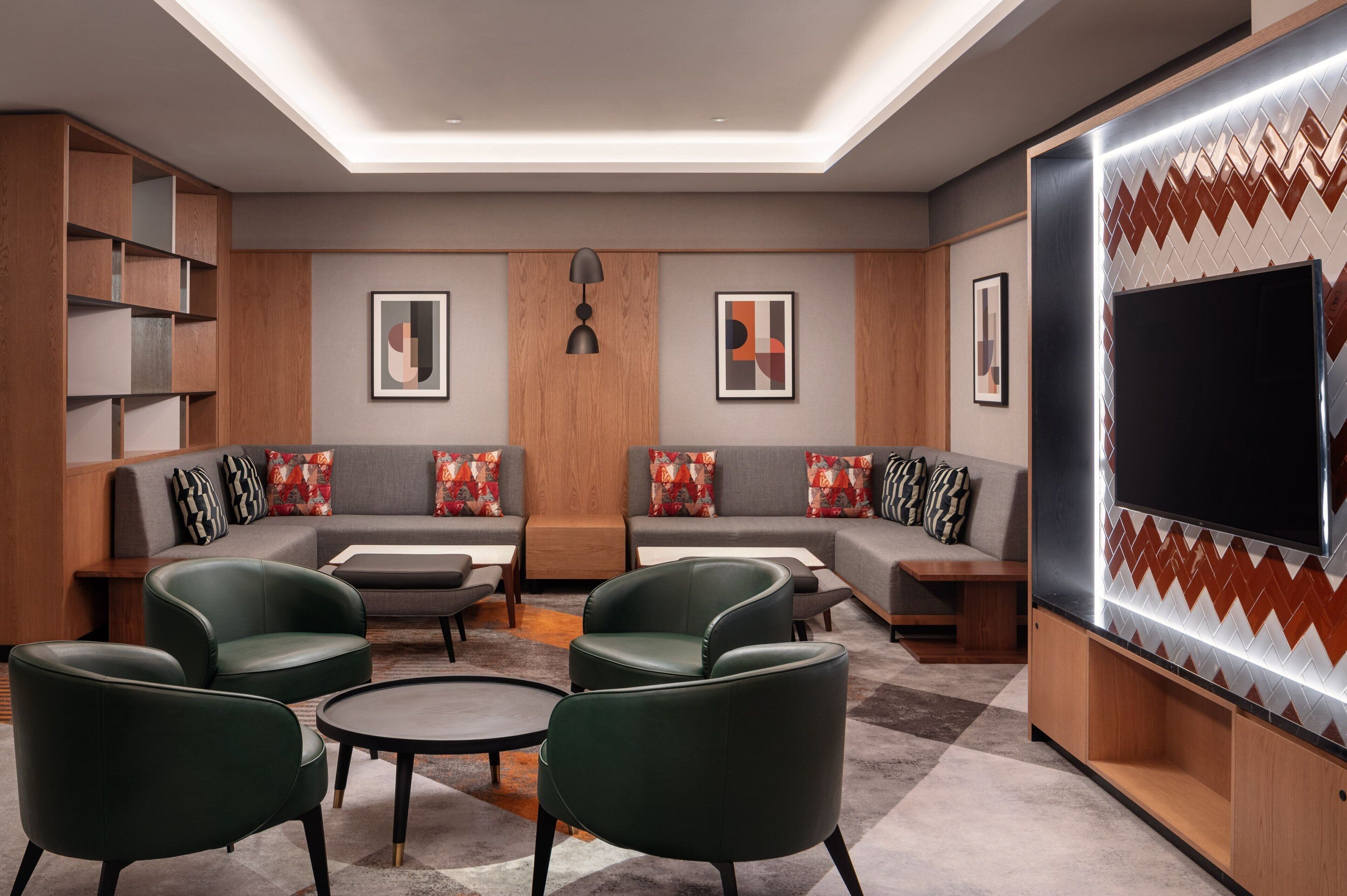 A modern living room with a sectional sofa, green armchairs, a coffee table, and a flat-screen TV mounted on a wall with a zigzag pattern.