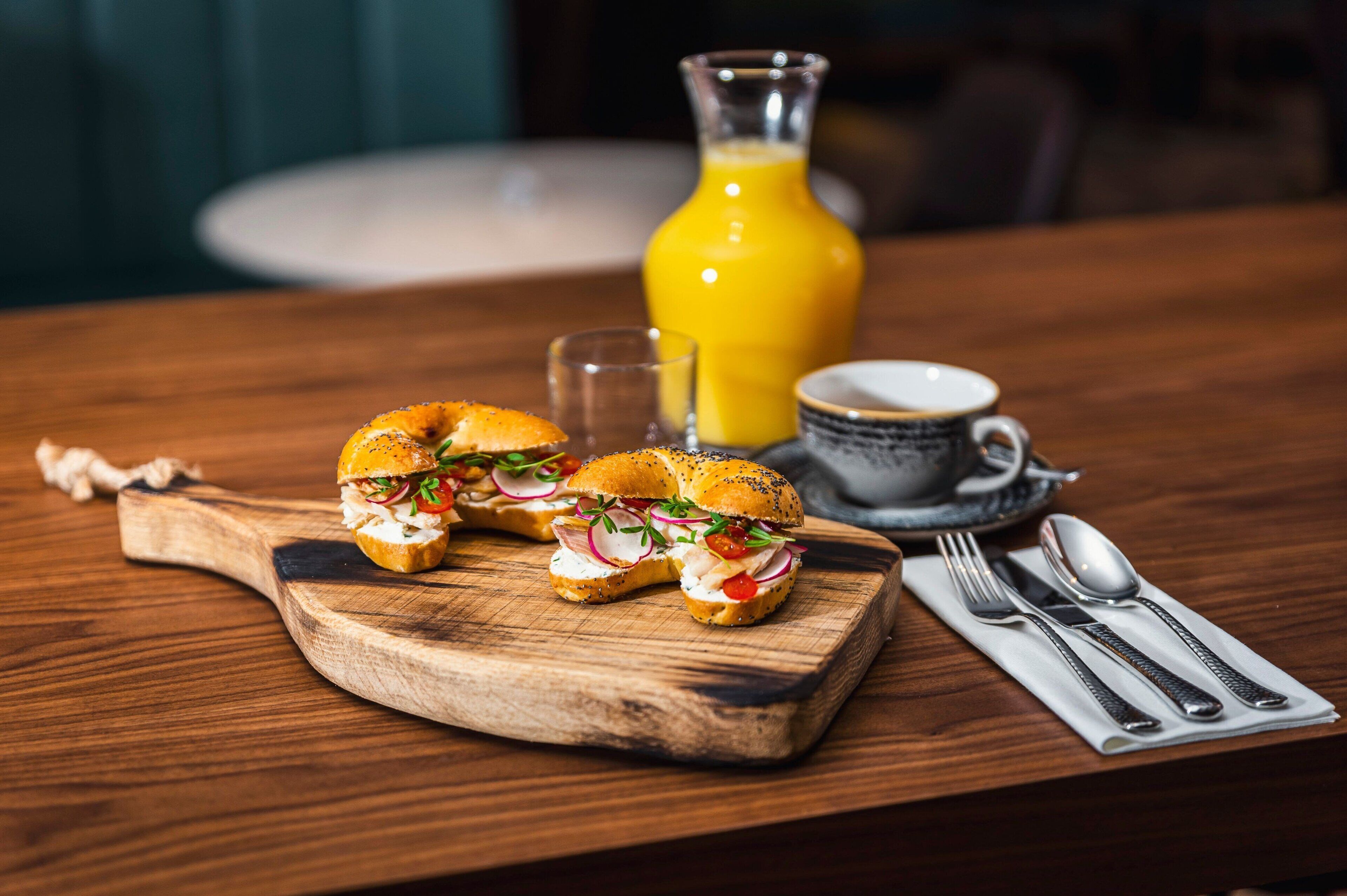 A wooden table with a cutting board holding a sandwich, a glass of orange juice, and a cup of coffee.