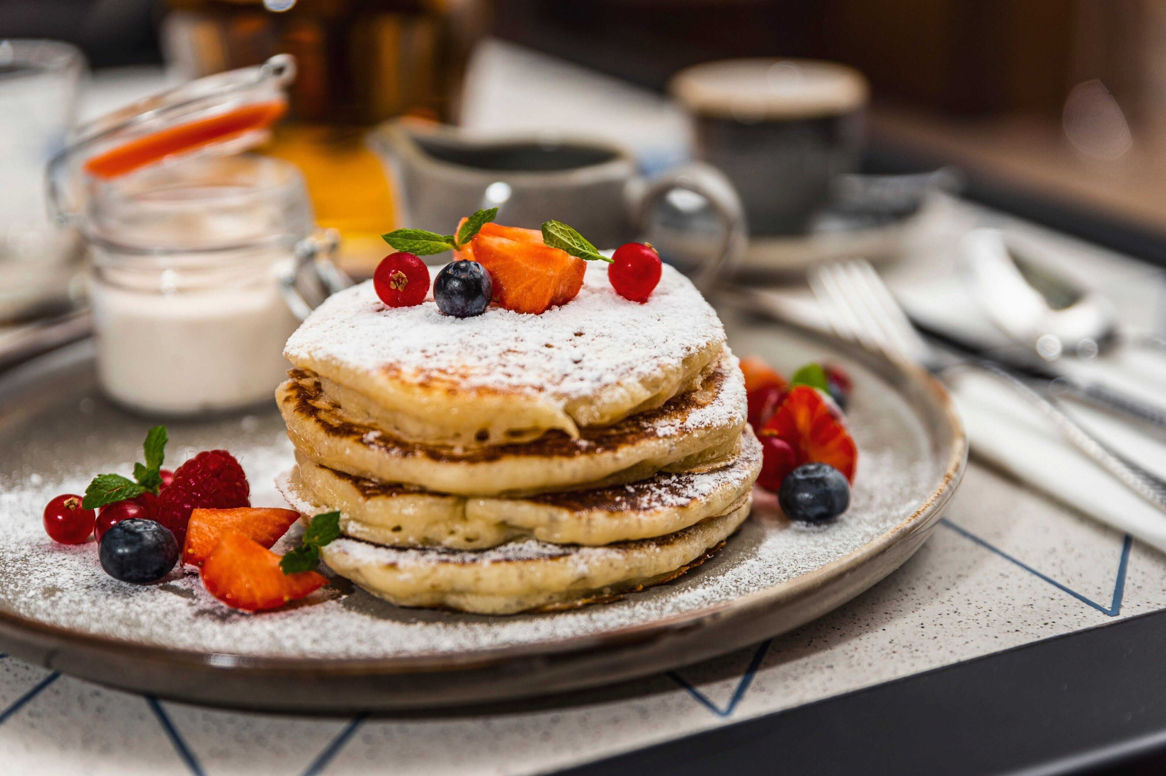 A stack of pancakes with fruit toppings on a plate, accompanied by a jar of milk and a cup of coffee.