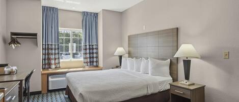Une chambre d’hôtel comprenant un lit, deux tables de chevet avec des lampes, un bureau avec une chaise, une fenêtre avec des rideaux et un radiateur fixé au mur.